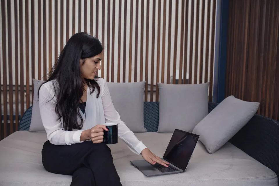 A woman working on a laptop on a sofa with a mug in her hand